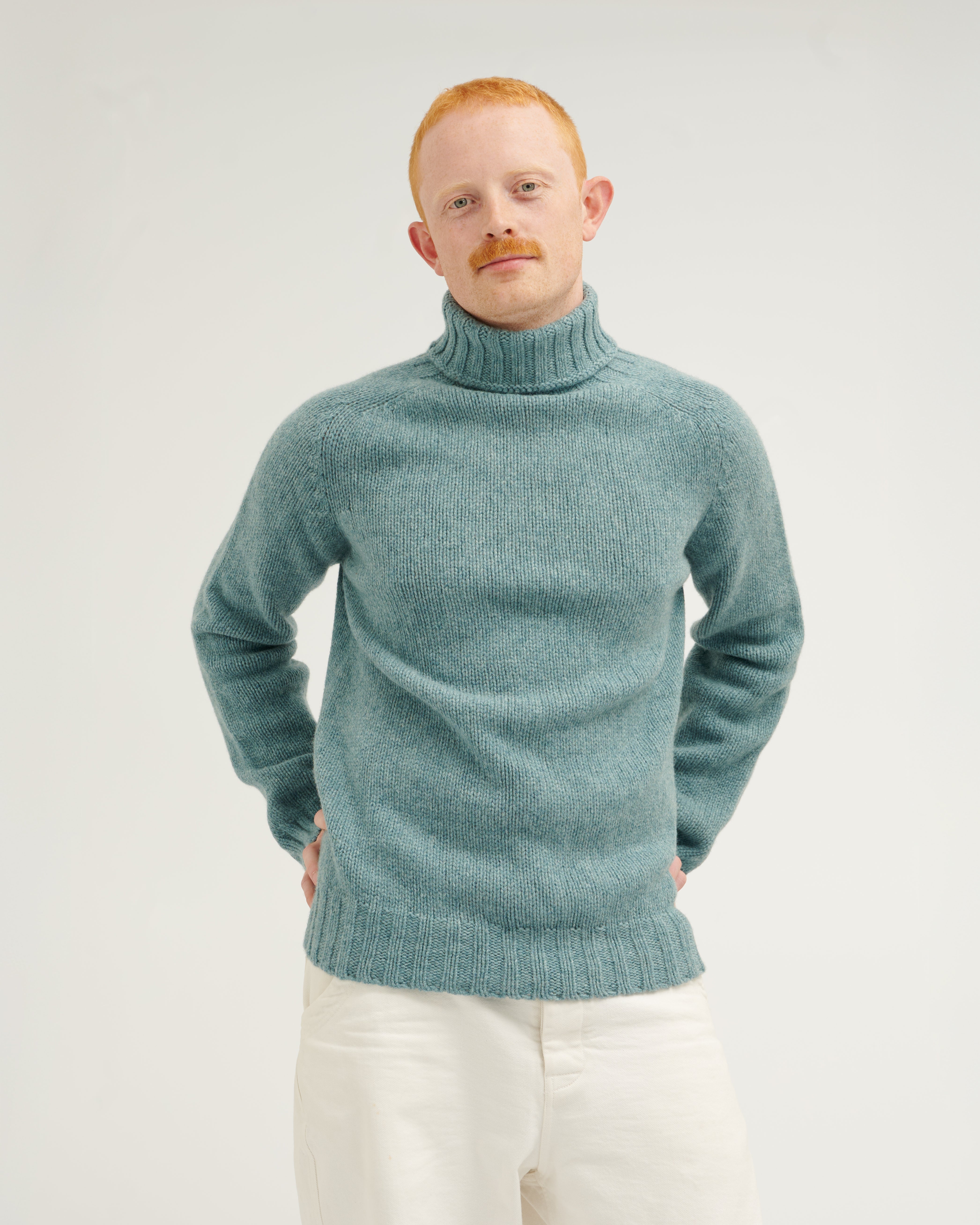 Man wearing a teal turtleneck sweater against a plain background