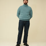 Man wearing a teal sweater and dark jeans on a beige background