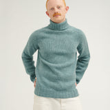 Man wearing a teal turtleneck sweater against a plain background